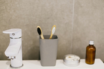 Bamboo toothbrush, ubtan for skin in glass bottle, solid shampoo in metal can, tonic on white sink in modern bathroom. Zero waste concept. Plastic free. Sustainable lifestyle