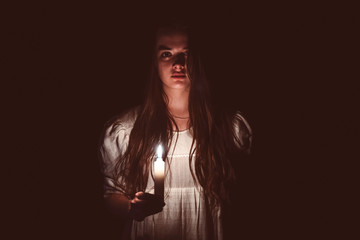 A young scary girl in an old white dress holding a candle in her hand and staring in to the camera....