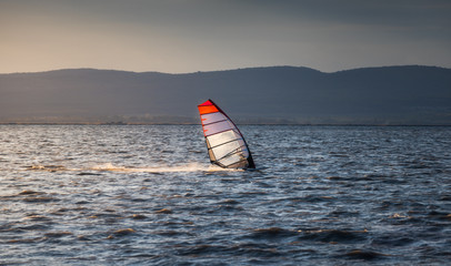 Windsurfer Surfing The Wind On Waves In Neusiedl Lake in Austria at Sunset. Recreational Water Sport. Summer Fun Adventure Activity.