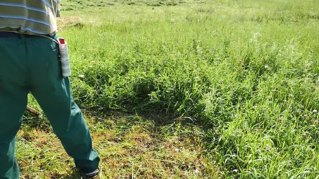 Slow motion footage of a farmer hand mowing the grass on a meadow with a scythe, the shot is folowing the grass mower...