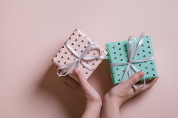 Female's hands holding gift boxes with ribbon on pink background. Valentine's day and birthday concept.