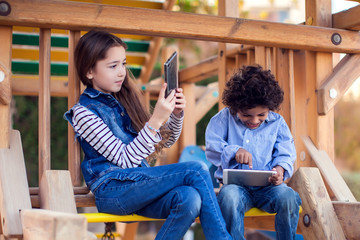 Two kids boy and girl playing with tablet outdoor. Children and gadget addiction concept