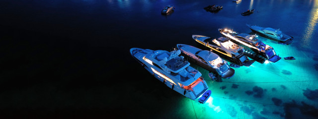 Aerial drone night shot of luxury yachts docked famous Psarou beach, Mykonos island, Cyclades,...