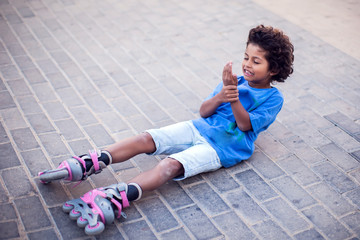 A kid boy on rollerskates fell down and feels pain. Children, activity and healthcare concept © Aleksej
