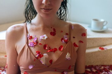 Close up female chest in beige bra with tropical flower petals relaxing in stone bath tube, organic skin care, luxury spa hotel, Bali Indonesia