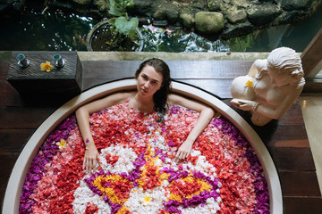 Woman relaxing in round outdoor bath with tropical flowers, organic skin care, luxury spa hotel, lifestyle photo, top view