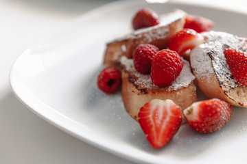 French toast with strawberries and raspberries, sprinkled with powdered sugar. Dessert on a white plate.