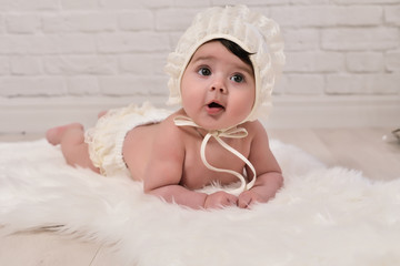 baby with white cap lying face down on a white blanket