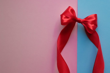 Bright red bow made from silk ribbon on blue and pink background. Festive concept with copy space....