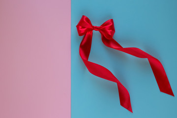 Bright red bow made from silk ribbon on blue background with copy space on pink background. Festive...