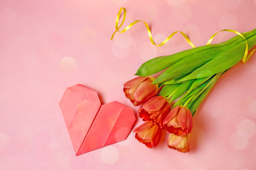 Holiday card with a red bouquet of tulips and a paper heart. Bouquet of tulips on a pink background. Top view, copy space, bokeh effect