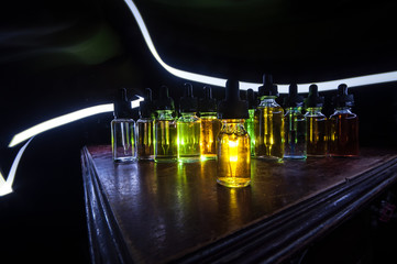 Smoke clouds and vape liquid bottles on dark background. Light effects. Useful as background or...