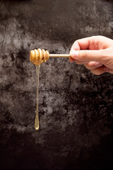 Spoon with honey in a hand on a dark background. Dripping fresh honey.