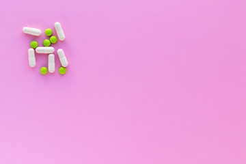 Green pills and white capsules isolated on pink background. Woman health. Epidemic, painkillers, healthcare and treatment concept. Flat lay. 