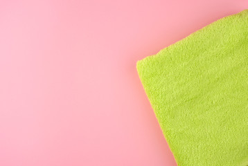 green cotton terry towel folded on a pink background, top view