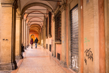 Couple walking in Bologna porticoes covered footpath in the  historical medieval centre of Bologna city. Emilia-Romagna region, Northern Italy.