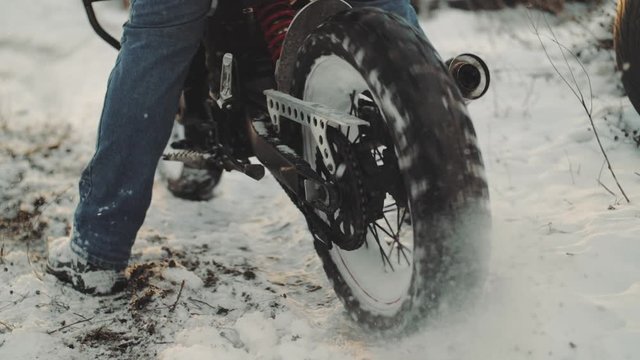 Motorcyclist doing tire burnout in the snow field, slow motion. Professional motorcyclist drift and turns on a motorcycle on the snow ground at sunset. Biker does a trick on a motorcycle 