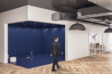 Businessman walking in blue office hall interior.