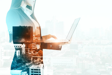Businesswoman silhouette using laptop on city background
