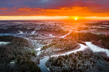 Stunning sunrise over valley surrounded with forest and river covered in snow. Scenic aerial landscape.