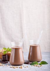 Organic non dairy soy chocolate milk in glass and wooden plate with soybeans on a gray concrete background.