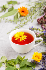 Cup of herbal tea with calendula, lavender, oregano, hyssop, mint and lemon balm on a gray concrete background. Side view, selective focus.