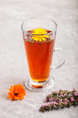 Glass of herbal tea with calendula and hyssop on a gray concrete background. Side view, close up.