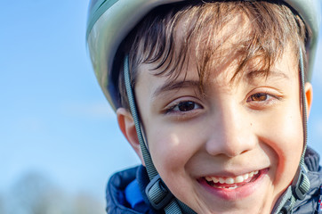 Portrait of a young boy outdoors wearing a bicycle helmet and smiling.