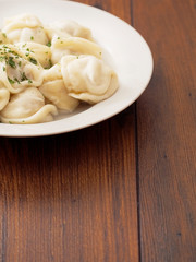 Portion of Russian traditional big size dumpling and herbs on a white plate and wooden table.