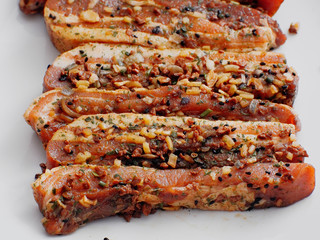 Tasty uncooked pork belly slices in soy marinade with herbs on a white plate. Close up.