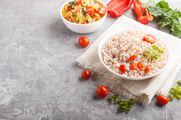 Unpolished rice porridge with stewed vegetables and oregano in white bowl on a gray concrete background. Side view, copy space.
