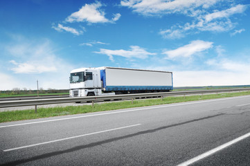 A big truck and trailer on the countryside road against a blue sky with clouds