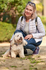 adult blond woman walking with fluffy white dog in city park