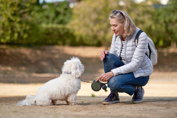 adult blond woman walking with fluffy white dog in city park