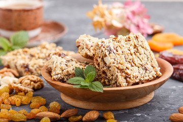 Homemade granola from oat flakes, dates, dried apricots, raisins, nuts with a cup of coffee on a black concrete background. Side view, selective focus