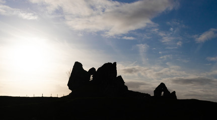 Backlight of some ruins of an old stone castle on a grassy hill in front of a large river....