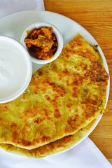 A plate with aloo paratha bread stuffed with potatoes and a dish of yogurt at an Indian restaurant