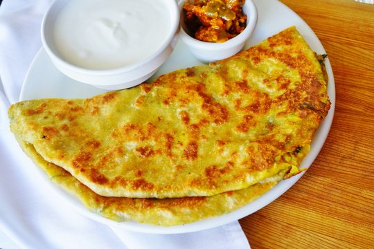 A plate with aloo paratha bread stuffed with potatoes and a dish of yogurt at an Indian restaurant