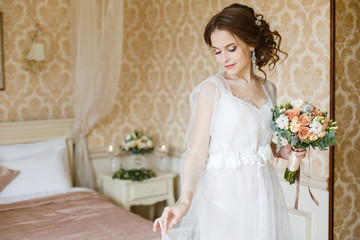 Pretty young Bride near or on a bed. Brown-haired woman with classic wedding hair-style. Boudoir morning of the bride. Romantic morning of Bride