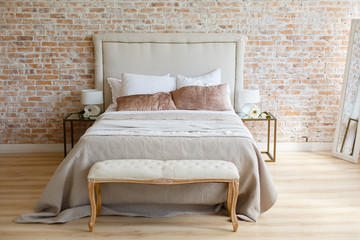 Stylish bedroom in loft style with light grey colors and wooden bed with grey blanket. Room in light loft stile with brick wall and light furniture. Comfortable bedroom. Combination of modern and old