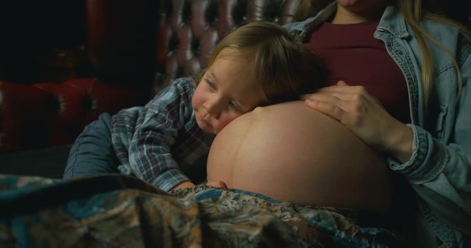 Preschooler resting his head on pregnant mother's belly