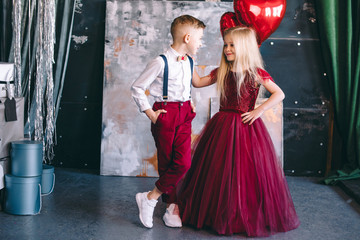 Happy little couple girl and boy with red hearts, red balloons, isolated on background. child boy and girl want to exchange hearts. St. Valentine's Day. Girl in luxury red dress. © Олег Кошевський