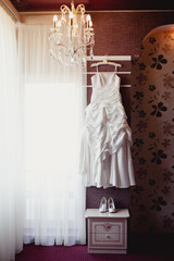Bridal accessories: wedding dress, shoes and bride's bouquet in a loght room. Bride's room in wedding day