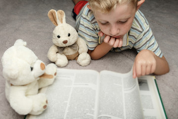 cute little boy reading book with his favorite toy