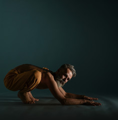 Old man with grey beard doing yoga, pilates, fitness training, stretching exercise, asana or balance workout on floor