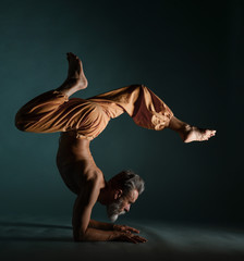 Old man with grey beard doing yoga, pilates, fitness training, stretching exercise, asana or...