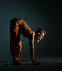 Old man with grey beard doing yoga, pilates, fitness training, stretching exercise, asana or...
