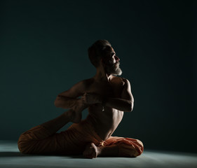 Old man with grey beard doing yoga, pilates, fitness training, stretching exercise, asana or balance workout on floor