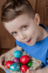 Fototapeta na wymiar Happy baby boy with a basket of easter eggs on wooden background