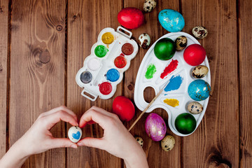 Hand painted Easter eggs, paints and brushes on wooden background. Preparation for the holiday. Girls hands draw a pattern